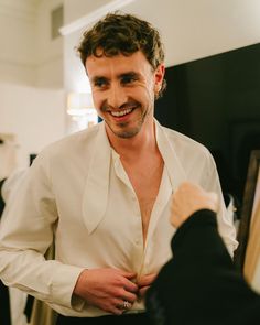 a man smiling and adjusting his shirt in front of a woman's dress coat