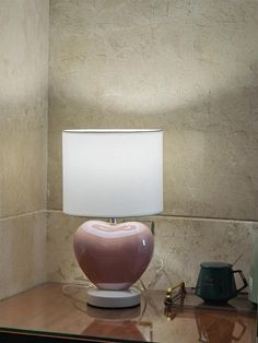 a pink lamp sitting on top of a glass table next to a white lamp shade