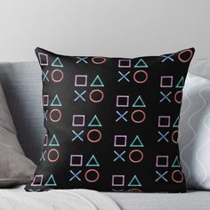 a black pillow sitting on top of a couch next to a white throw pillow with pink, blue and green symbols