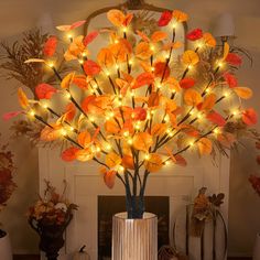 a lighted tree with orange leaves in front of a fireplace