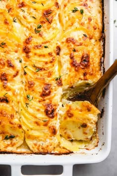 a casserole dish with potatoes and cheese in a white baking dish, topped with a wooden spoon