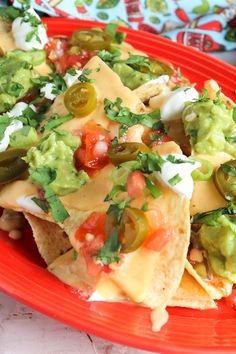 nachos with guacamole, tomatoes and peppers on a red plate