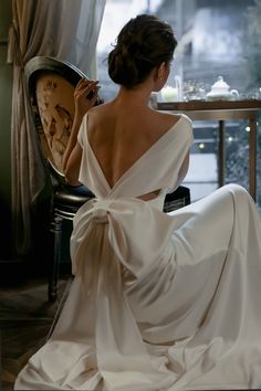 a woman in a white dress sitting on a chair with her back to the camera