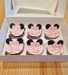 cupcakes with pink frosting and minnie mouse ears in a white box on a wooden table