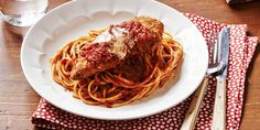 a white plate topped with spaghetti and meat covered in marinara sauce next to a glass of water