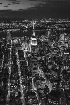 black and white photo of new york city at night with the empire building lit up