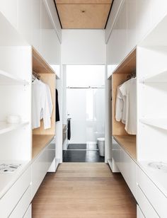 an empty walk - in closet with white cabinets and wood flooring on the walls