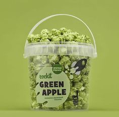 a plastic bucket filled with green apples on top of a green background, next to a black and white mouse