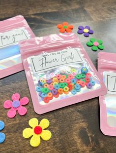 three plastic bags filled with different colored buttons on top of a wooden table next to flowers