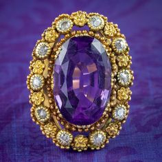 An impressive antique Victorian statement ring built around a large oval cut amethyst in the centre, weighing approx. 7.2 carats. It has a deep, regal purple hue and is framed in an ornate, cannetille style gallery encircled with gold beading, forget me nots and ten old mine cut diamonds, totalling approx. 0.50ct.  Amethyst is the birthstone of February and is considered a stone of protection, clarity and tranquillity. Its deep violet colouring has been highly esteemed throughout history, adorni Victorian Style Oval Purple Amethyst Ring, Victorian Style Purple Oval Amethyst Ring, Antique Oval Purple Amethyst Ring, Antique Oval Amethyst Ring, Victorian Oval Amethyst Ring With 17 Jewels, Oval Purple Amethyst Ring With 17 Jewels, Antique Oval Amethyst Ring With Center Stone, Victorian Amethyst Ring With Oval Center Stone, Amethyst Ring With Rose Cut Diamonds, Oval Shape