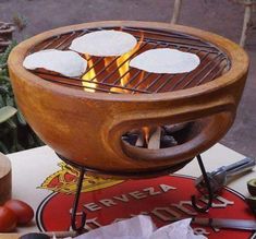 three tortillas cooking on an outdoor grill with flames in the center and other food items around it