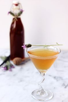 a drink in a martini glass on a marble table with a bottle and flowers behind it