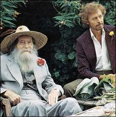 two men sitting next to each other in front of trees and bushes, one with a long white beard