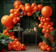 an orange balloon arch with greenery and potted plants on the side table in front of it