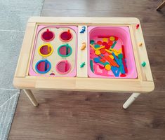 a child's wooden table with two trays filled with toys on top of it