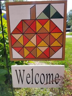 a welcome sign with an apple on it in front of some grass and bushes,