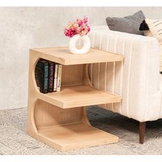 a small wooden shelf with books on it next to a white chair and flower vase