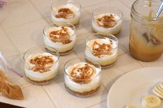 small desserts are arranged on a table with bananas and other foods in glass dishes