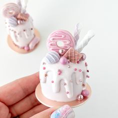 a hand holding a miniature cake with pink and white decorations on it's top