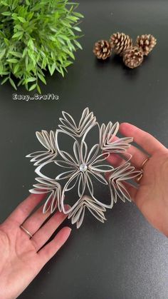 a hand holding a metal snowflake on top of a table next to pine cones