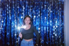 a woman standing in front of a blue curtain holding a sparkle wand