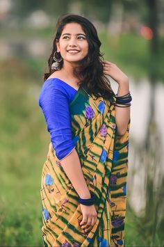 a woman standing in the grass wearing a yellow and blue sari