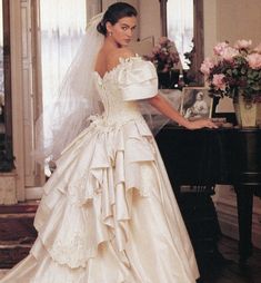 a woman standing next to a piano wearing a wedding dress with ruffles on it