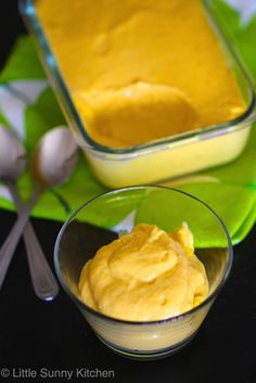 two bowls filled with yellow pudding on top of a green napkin next to spoons