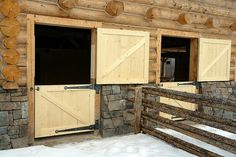 two wooden doors are open on the outside of a log cabin with snow around them