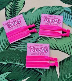 three pink hair ties with the words bestie on them and palm leaves in the background