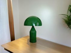 a green lamp sitting on top of a wooden table next to a potted plant