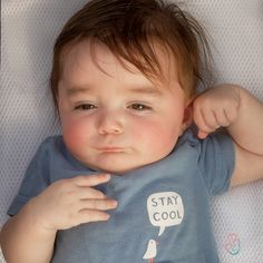 a small child laying on top of a bed wearing a t - shirt that says stay cool