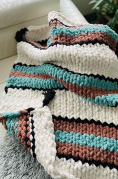 a crocheted blanket sitting on top of a couch next to a potted plant