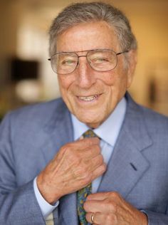 an older man wearing glasses and a blue suit is adjusting his tie with his hands