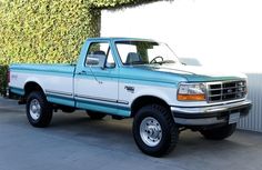 a blue and white pickup truck parked in front of a green plant covered wall with ivy growing on it's side