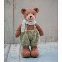 a stuffed teddy bear wearing overalls and a scarf is sitting on the ground in front of a door