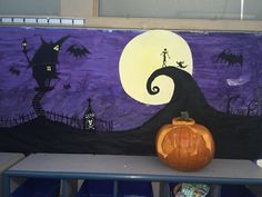 a pumpkin sitting on top of a table in front of a halloween scene painted on the wall