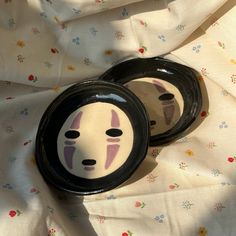 two black and white plates with faces painted on them sitting on a floral print cloth