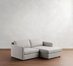 a gray couch sitting on top of a wooden floor next to a white painted wall