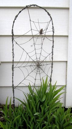 a metal spider web sitting on top of a lush green plant next to a white house