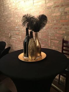 three vases with feathers sit on top of a round black table in front of a brick wall