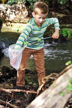 a young boy standing on the edge of a river holding a plastic bag