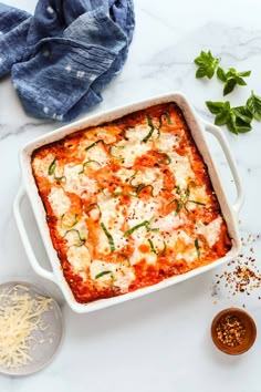 a casserole dish with cheese, sauce and herbs next to it on a marble countertop