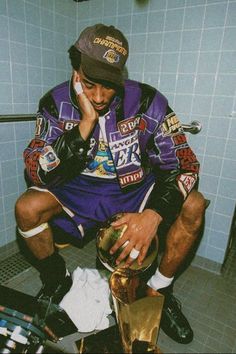 a man sitting on top of a toilet in a bathroom next to a trash can