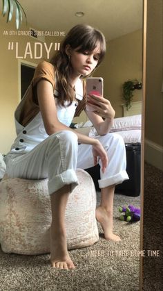 a woman sitting on a bean bag chair looking at her cell phone in front of a mirror