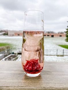 a glass filled with liquid sitting on top of a wooden table next to a lake