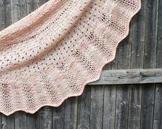 a pink crocheted shawl hanging on a wooden fence next to a piece of wood