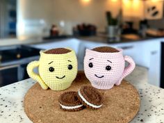 two crocheted coffee mugs sitting on top of a cork coaster