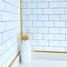 a white vase with flowers in it sitting on the floor next to a tiled wall