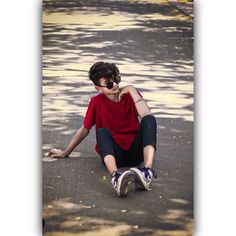 a young man sitting on the ground with his legs crossed, wearing sunglasses and a red shirt